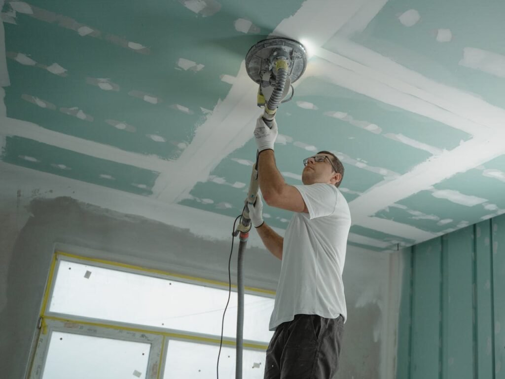 Professional Melbourne builder on scaffolding sanding plastered ceiling during home renovation project